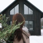 Home Preparation - a woman standing in front of a house holding a christmas tree