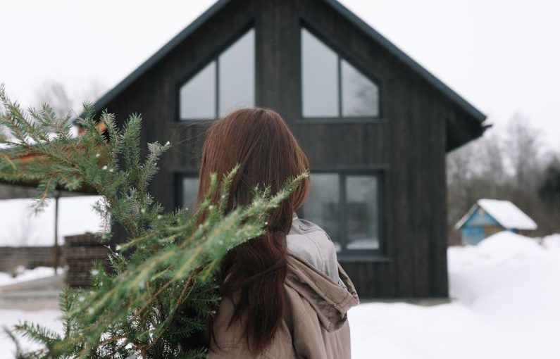 Home Preparation - a woman standing in front of a house holding a christmas tree