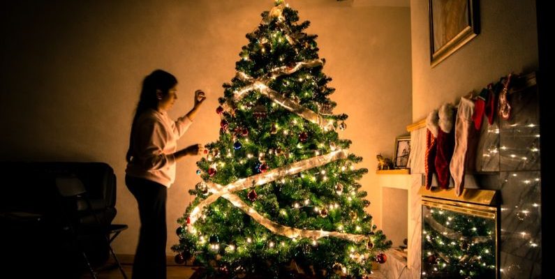 Decorating Budget - child standing in front of Christmas tree with string lights